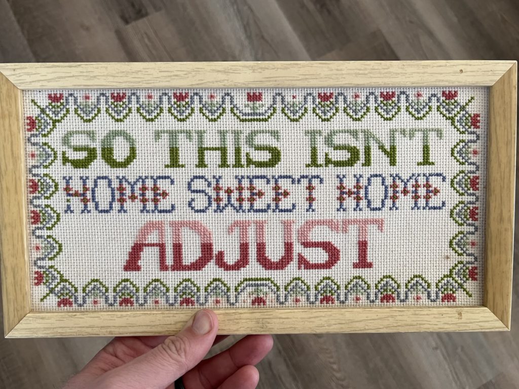 A handstitched sign that says so this isn’t home sweet home adjust.